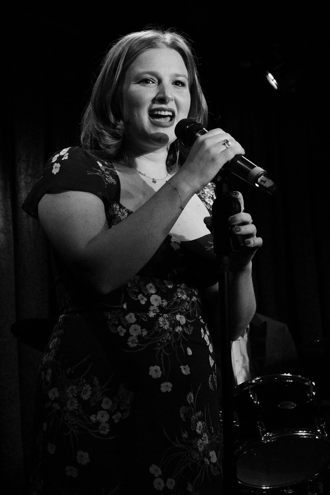 The singer in a floral dress at the microphone, in black and white.