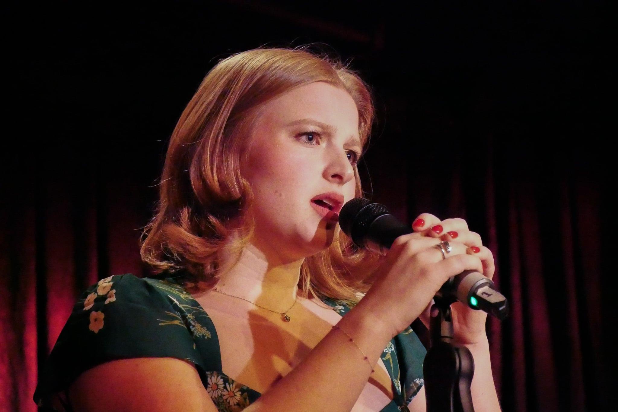 The singer holding the microphone with both hands, lit warm against the dark.