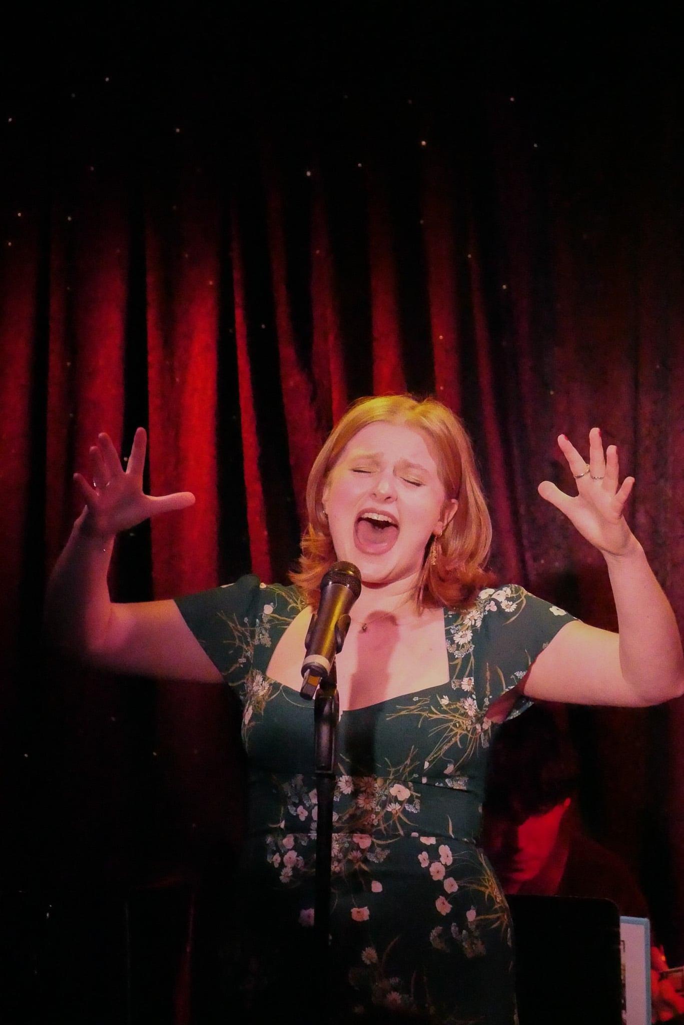 The singer with both hands raised, lit red against the curtain.