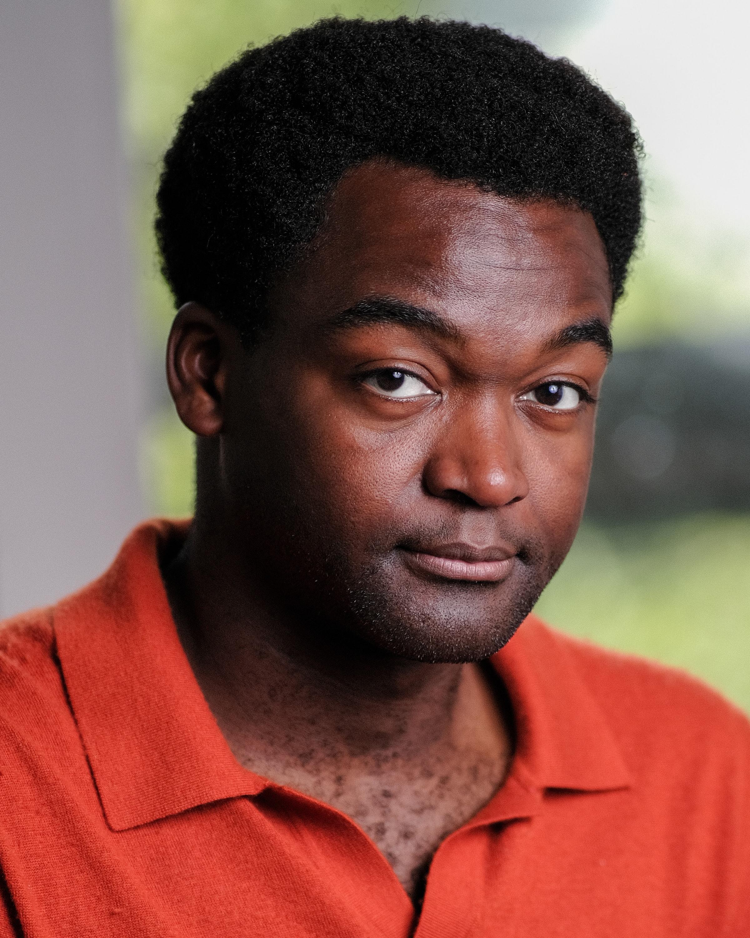 Man in a red polo shirt beside a window, looking just past the camera.