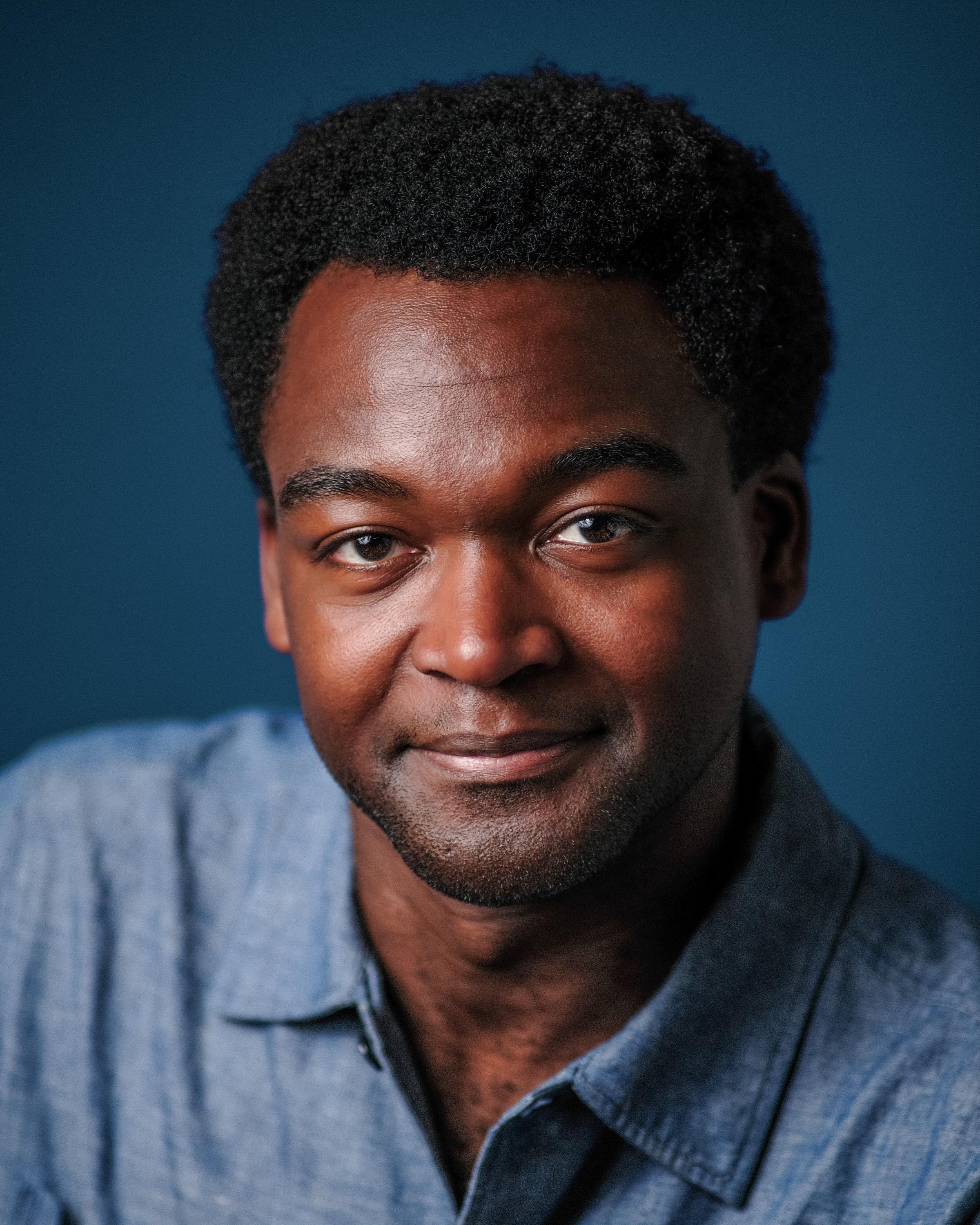 The same man, closer, smiling against a deep teal backdrop.