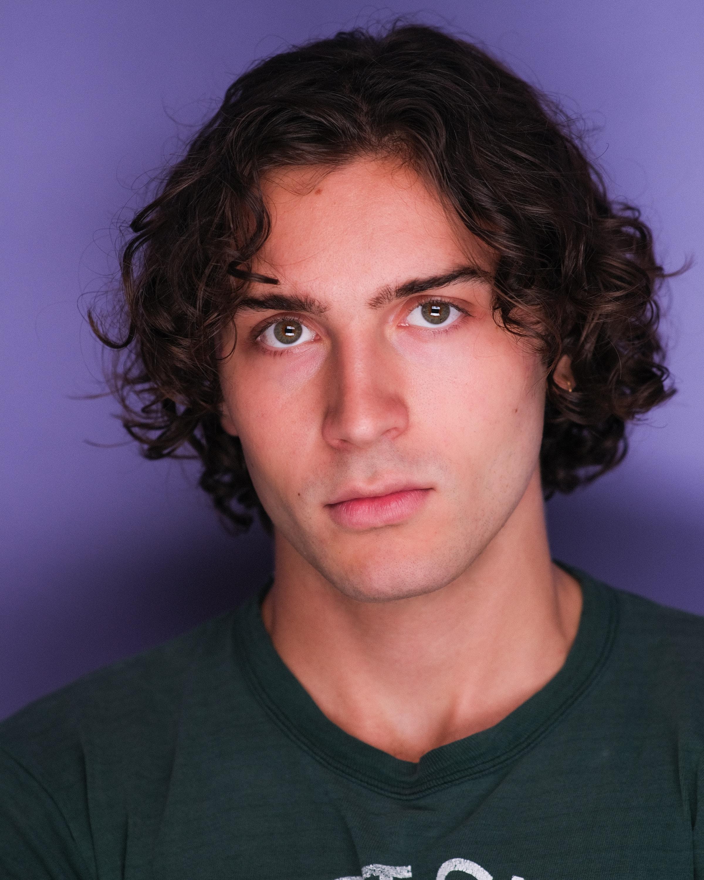 The same man in a dark green T-shirt against a violet backdrop.