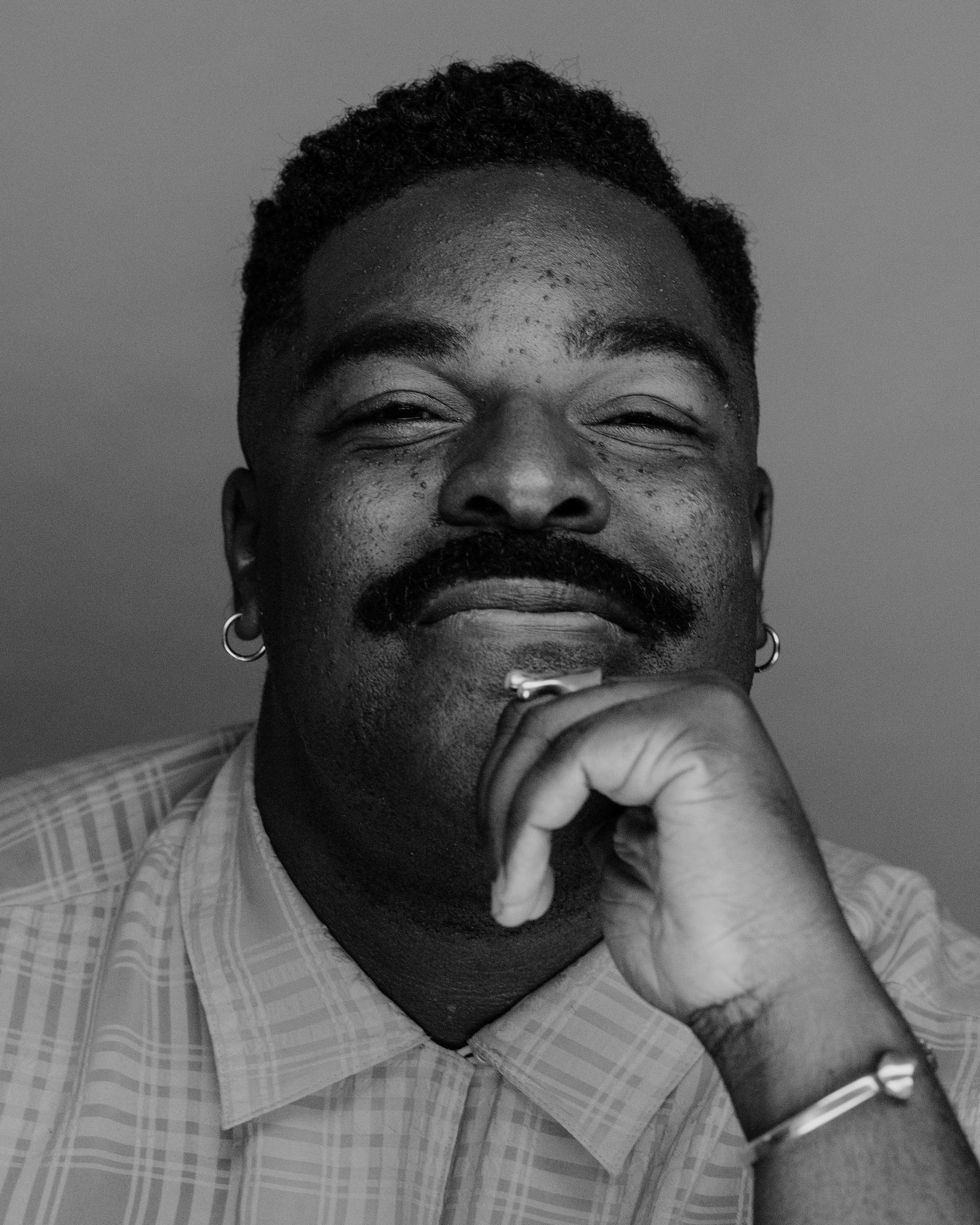 The same man in black and white, eyes creased in a smile, chin resting on his hand.