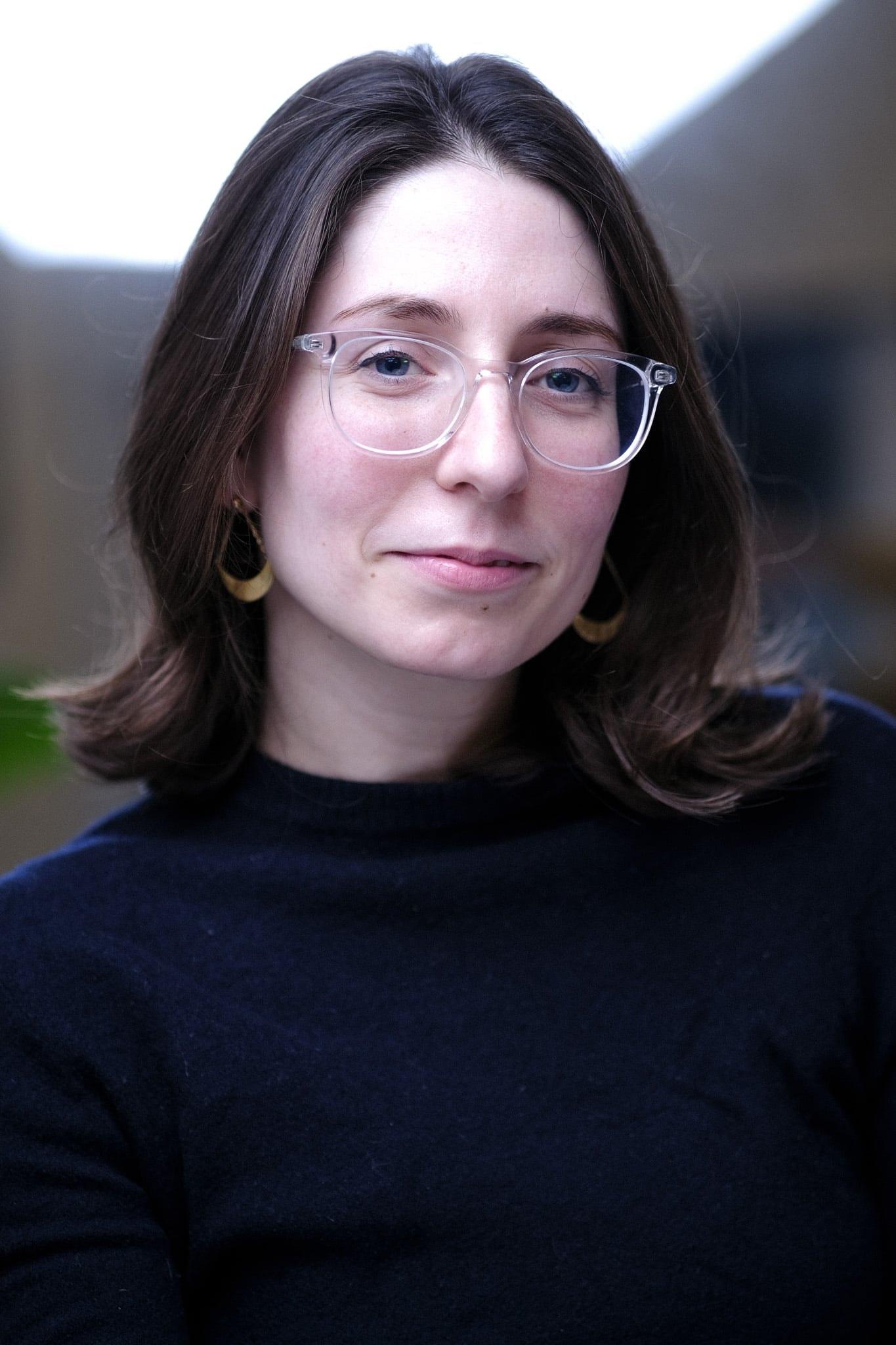 The same woman in clear-framed glasses against a bright window.