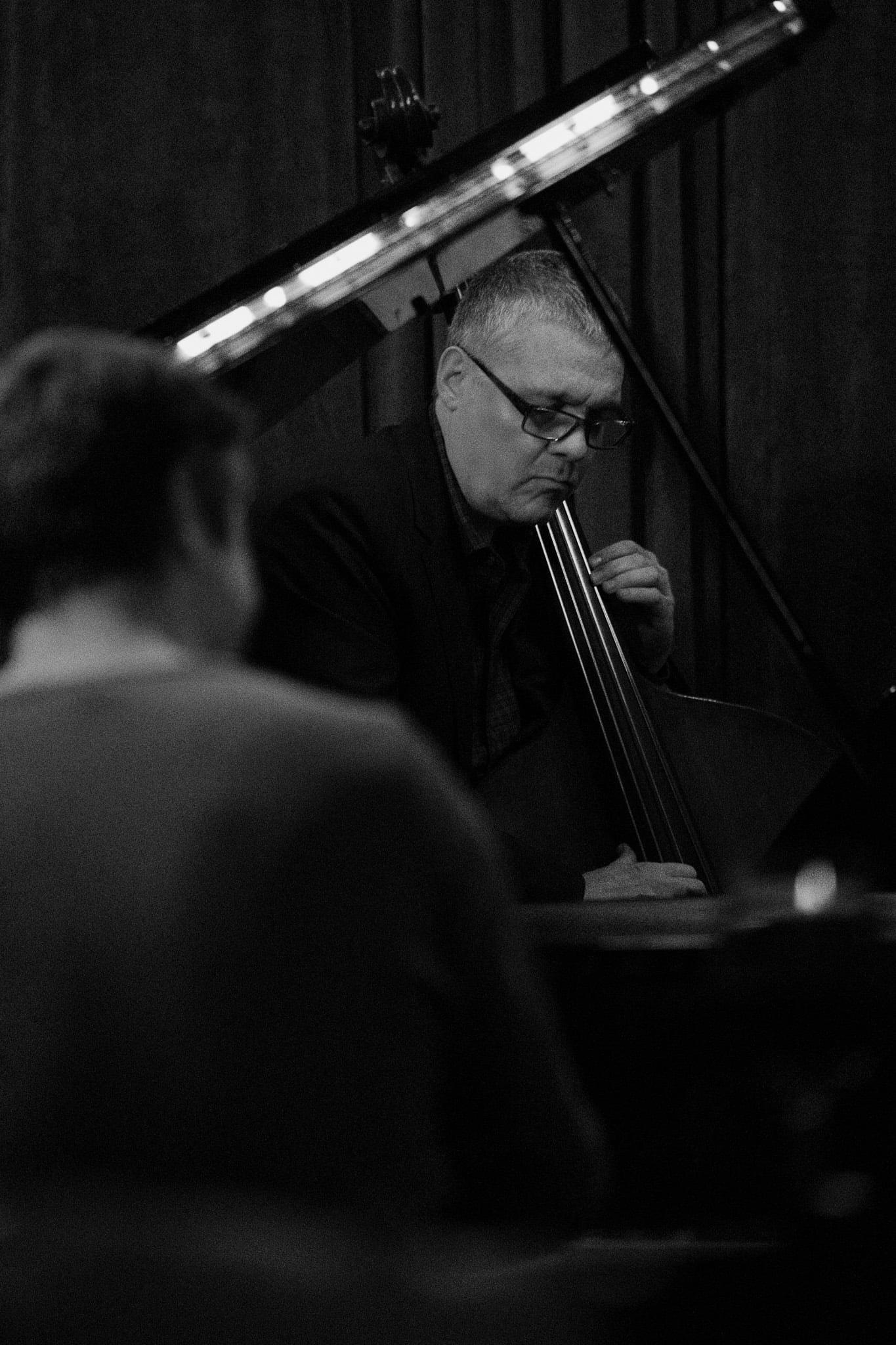 A bassist behind the curve of a piano lid, in black and white.