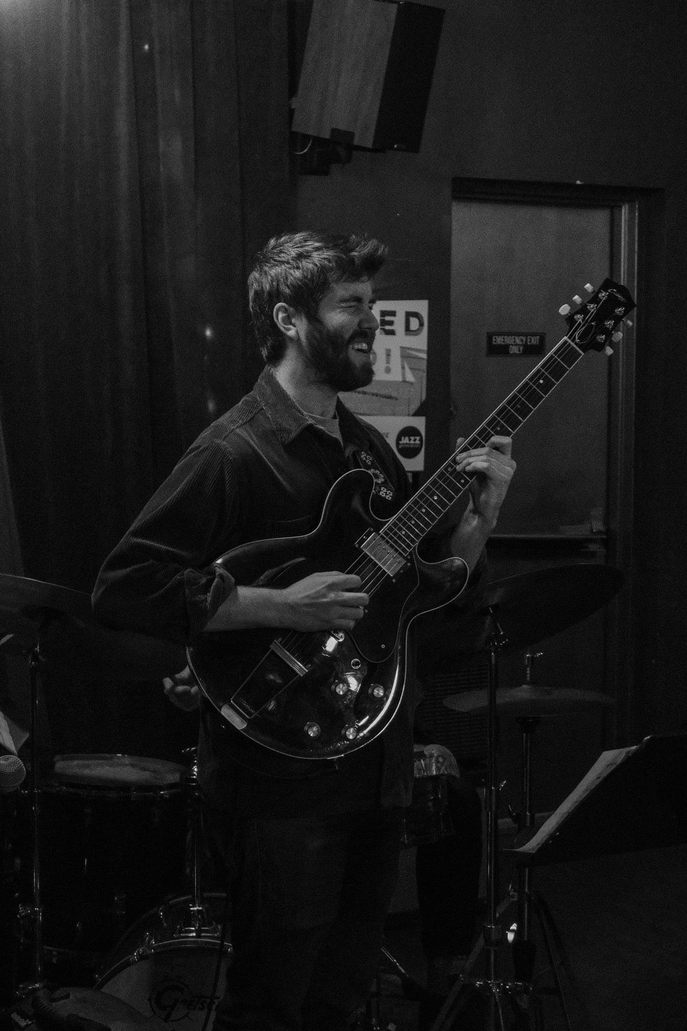 A guitarist looking down at his hands on the fretboard, in black and white.