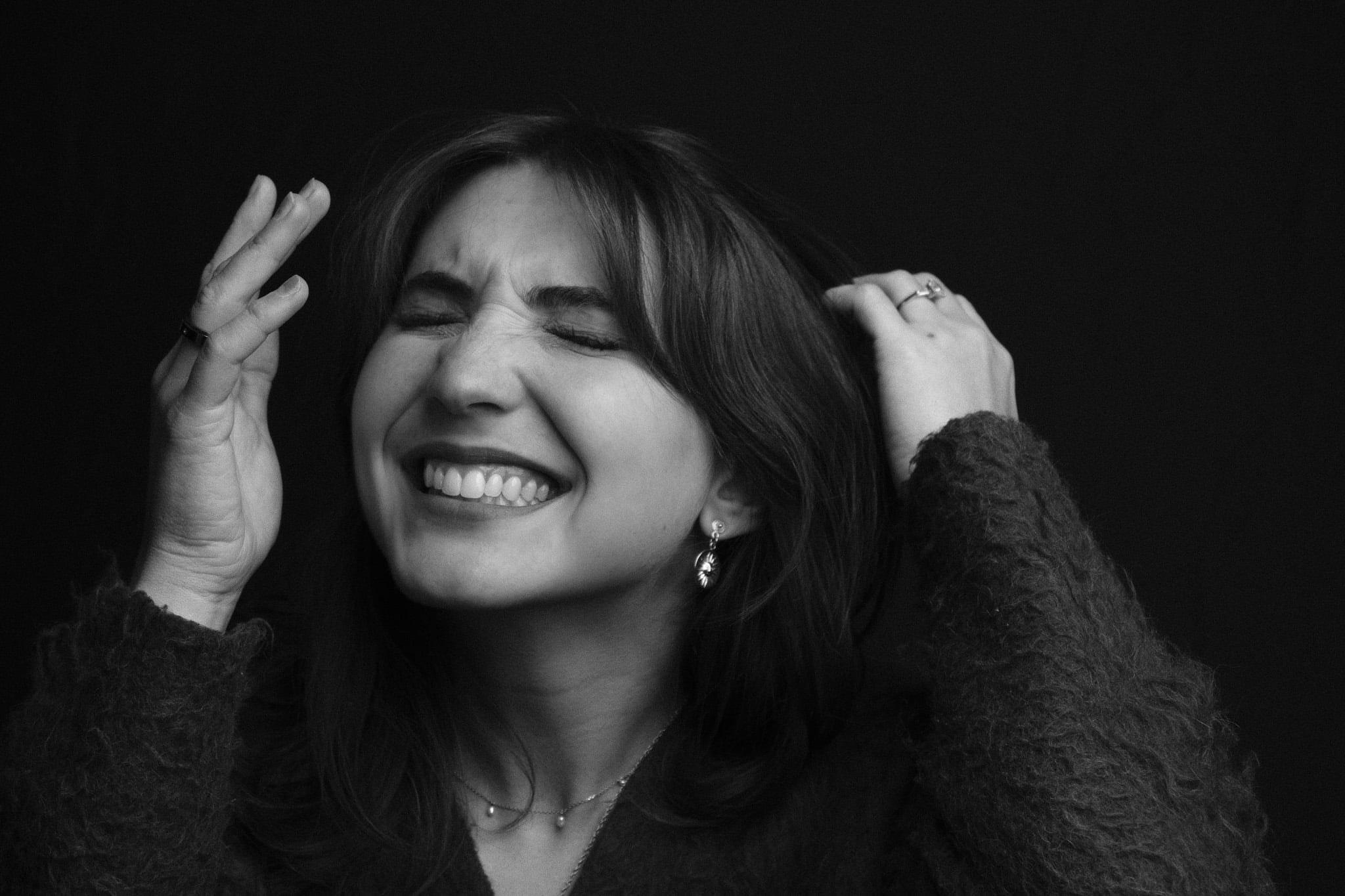 A woman laughing with her eyes shut and hands in her hair, in black and white.