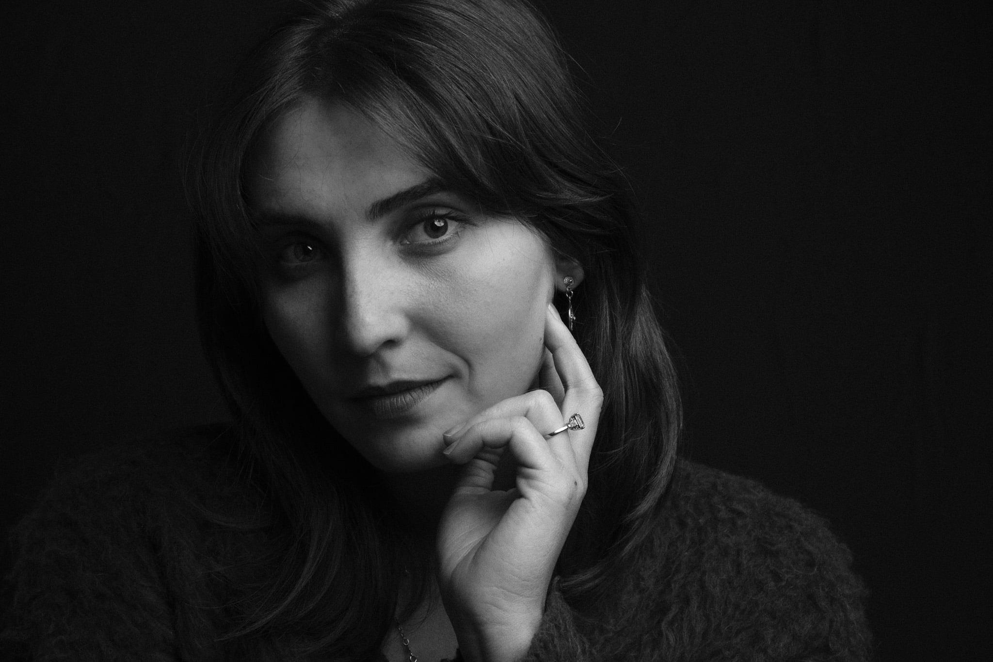 The same woman, chin resting on her hand, looking into the lens.