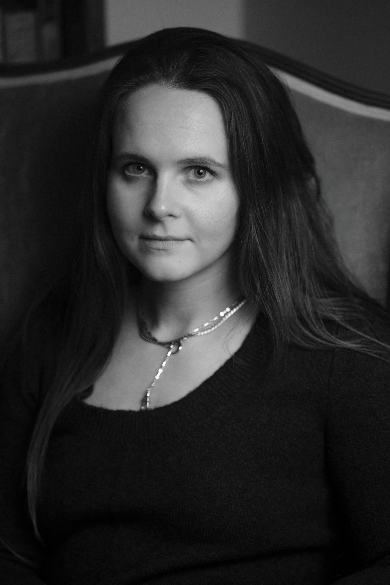 A woman with long straight hair and a pendant necklace, in black and white.