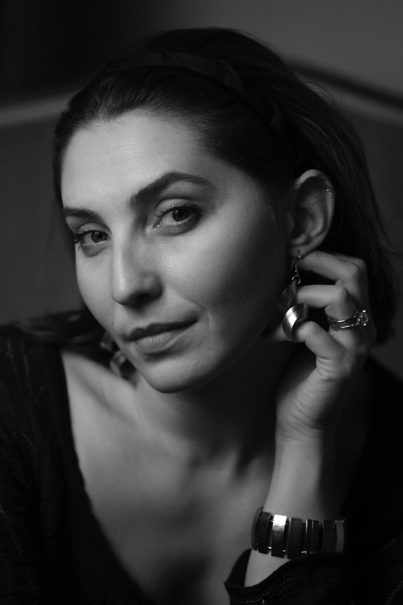 A woman touching her earring, looking to one side, in black and white.
