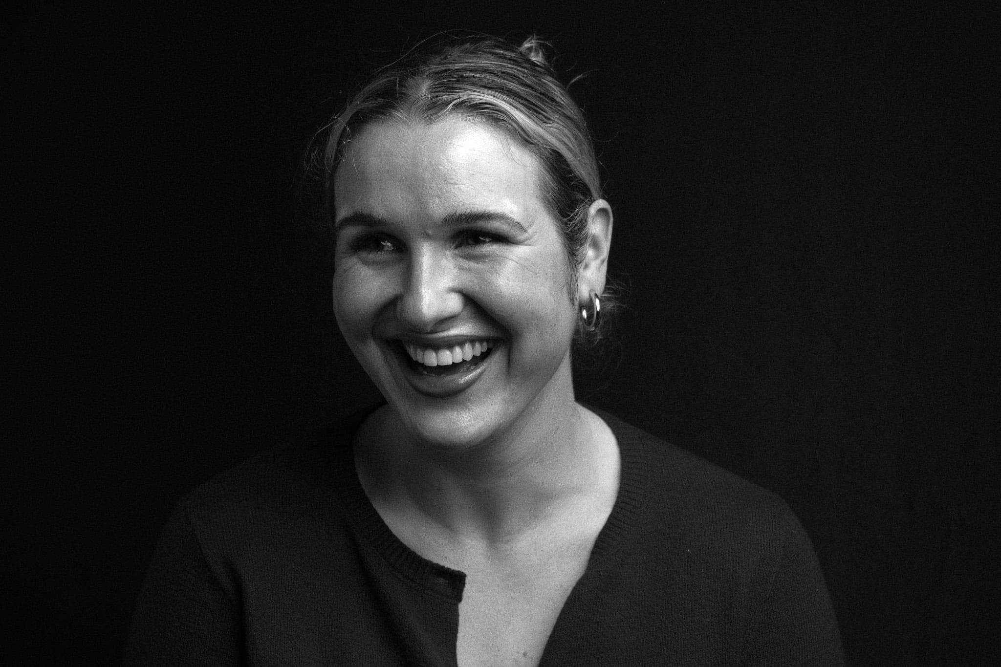 The woman alone, laughing, hair pulled back, against a black backdrop.