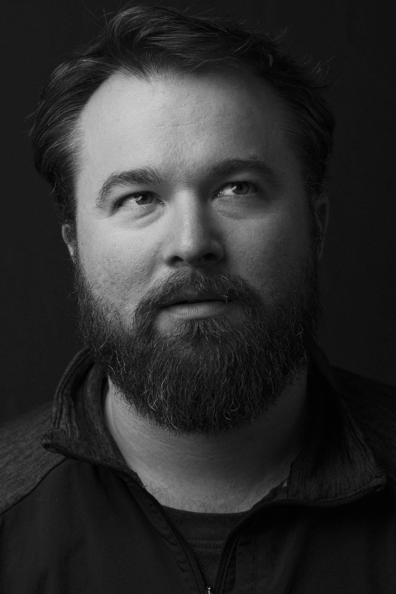 A bearded man looking up and off to the side, in black and white.