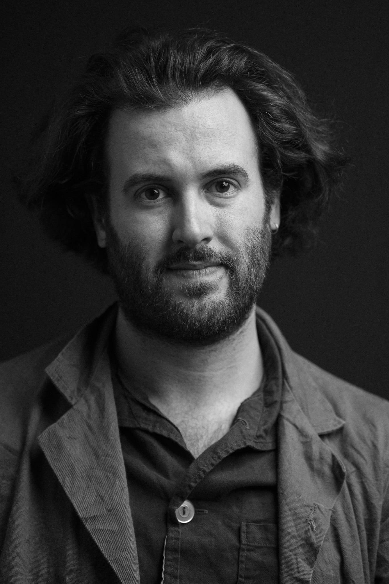 A man with wavy hair in a work jacket, in black and white.