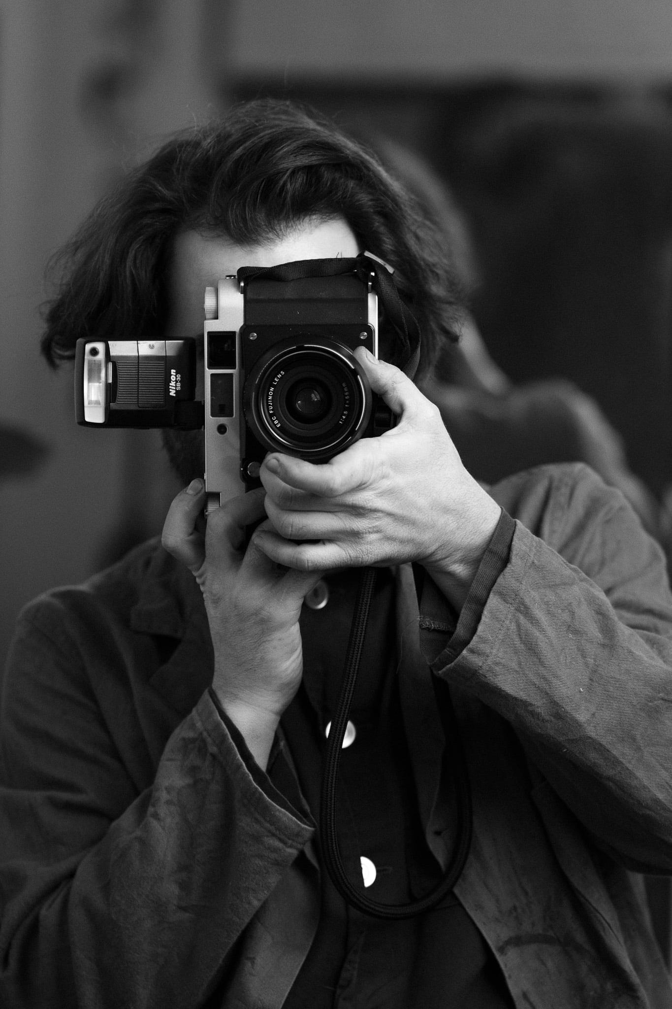 A man holding a medium format camera up to his face, in black and white.