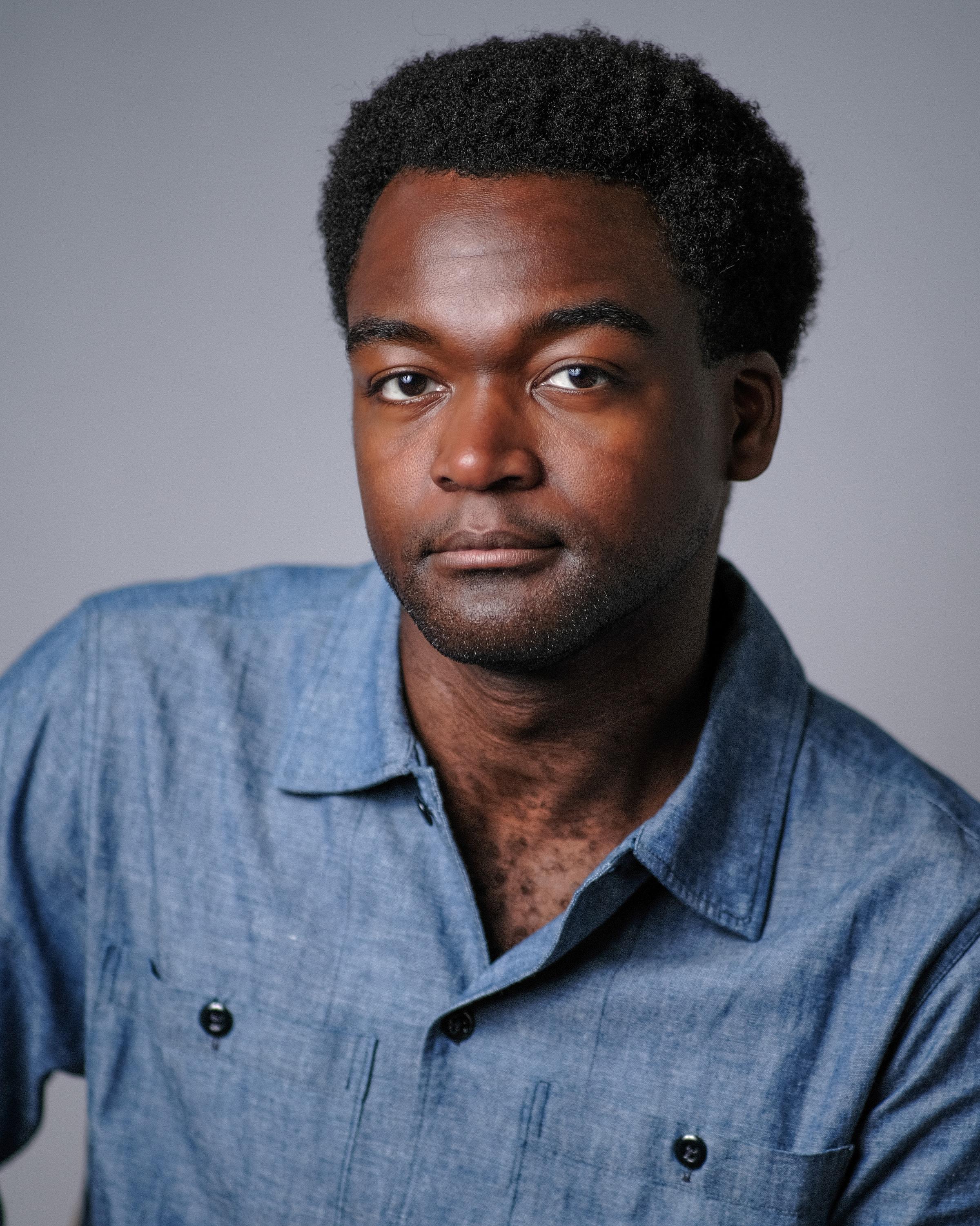 A man in a chambray shirt against a grey backdrop.