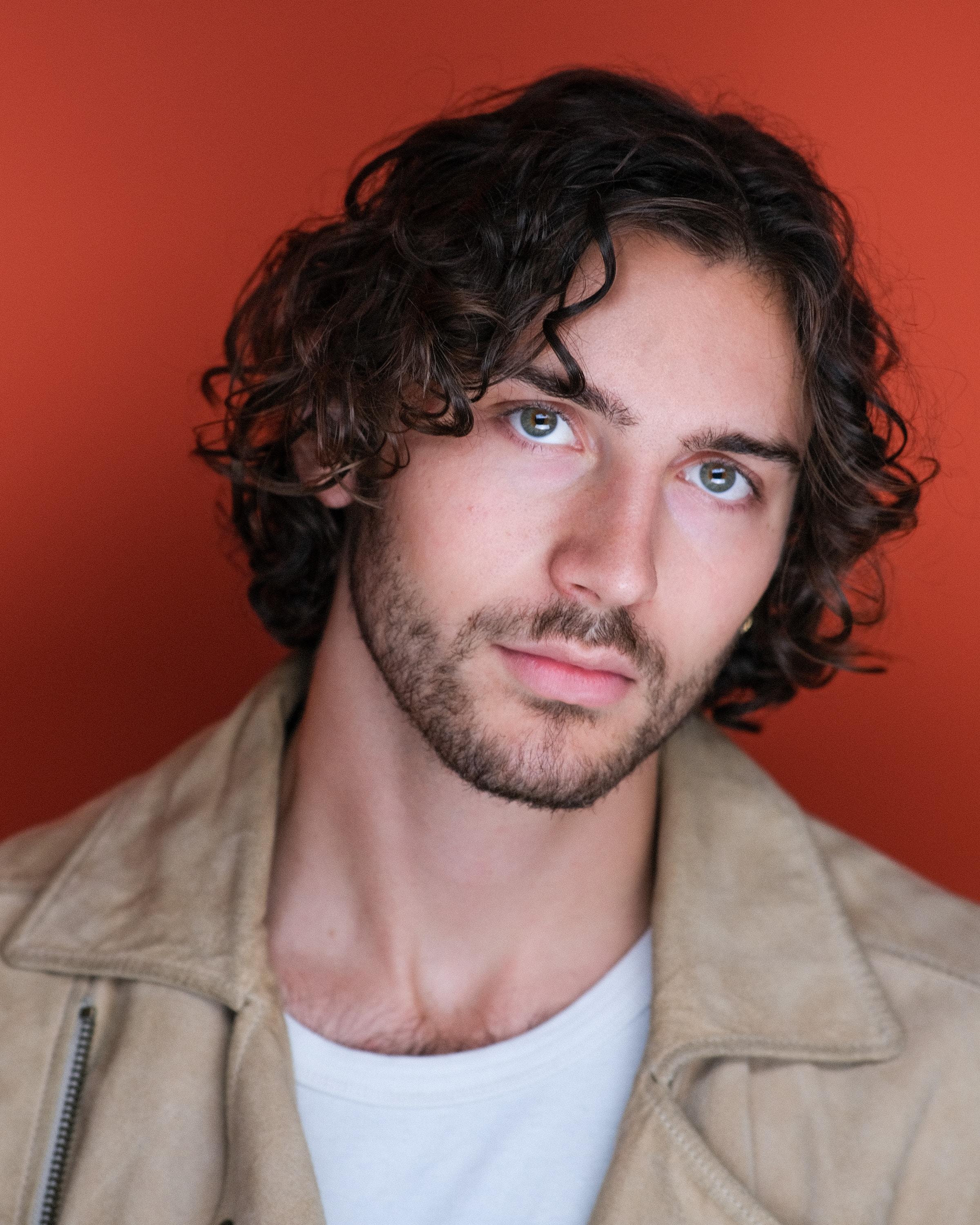 A man in a tan suede jacket against an orange backdrop.