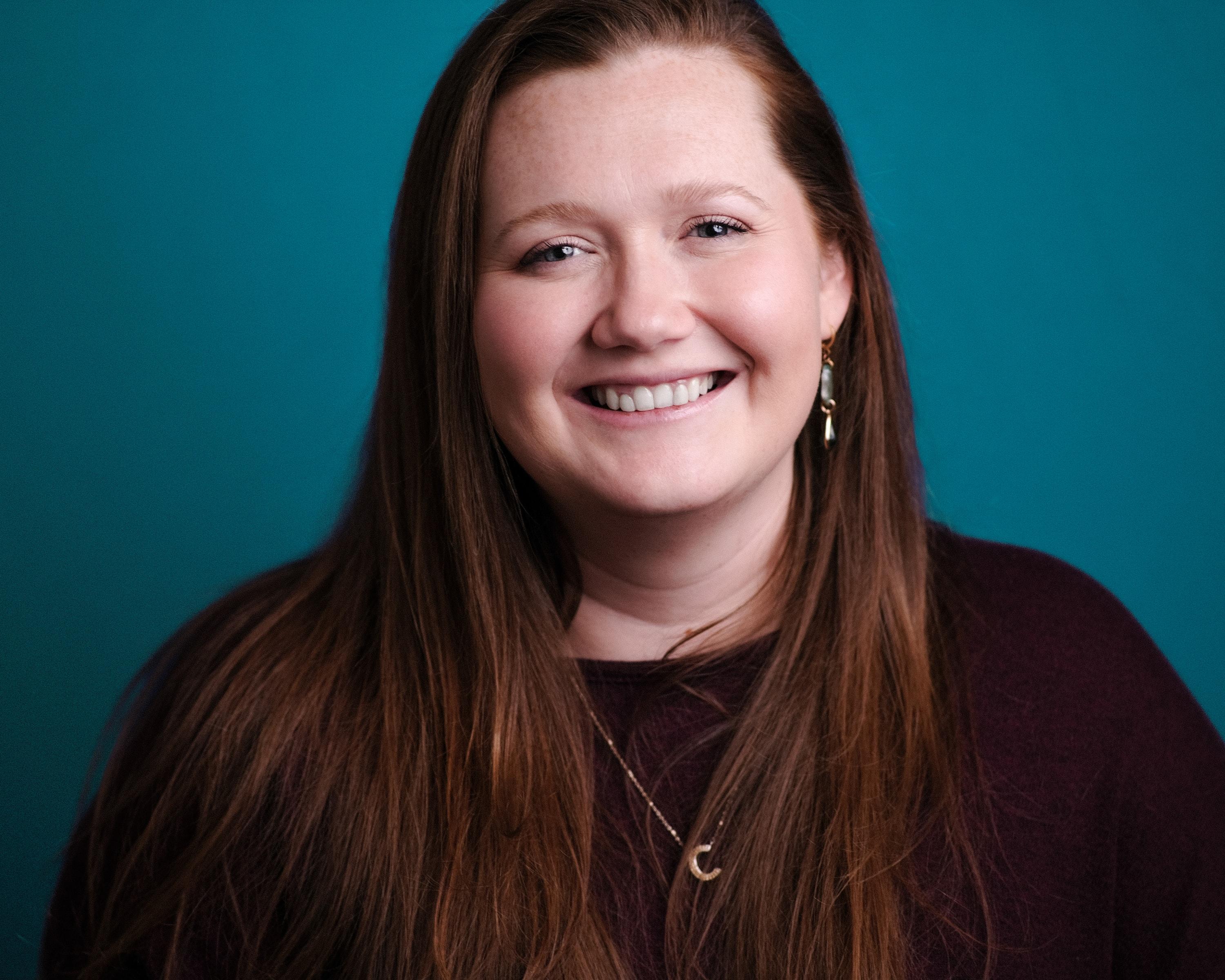 A woman laughing against a bright teal backdrop.