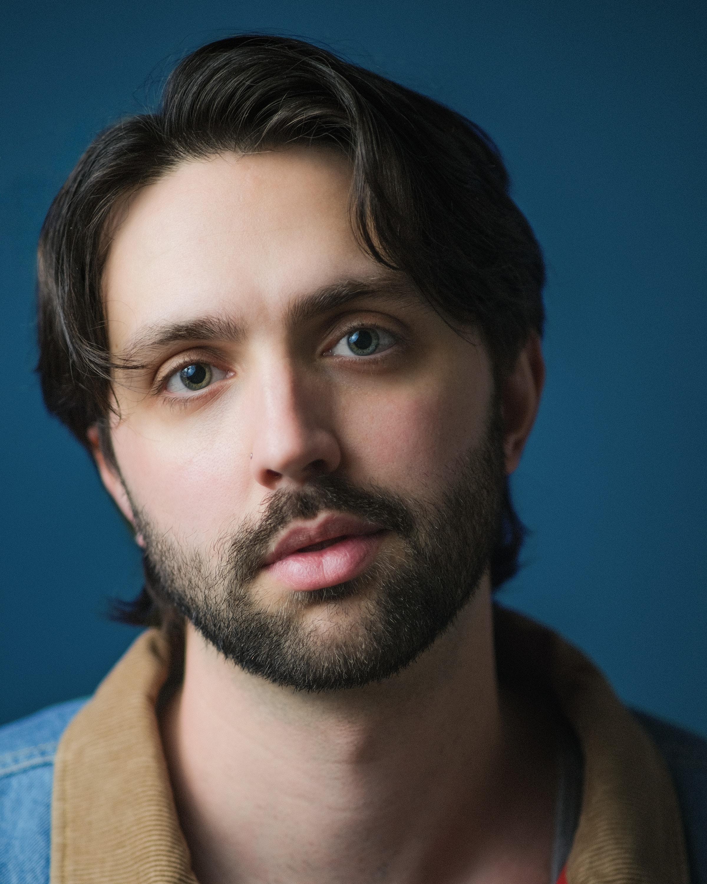 Shane Lonergan, with dark hair and a beard, against a blue backdrop.