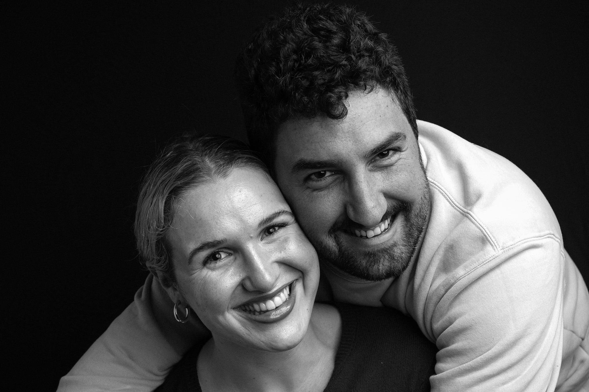 A couple laughing, his arms around her, in black and white.